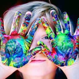 Child playing in paint shows hands to camera