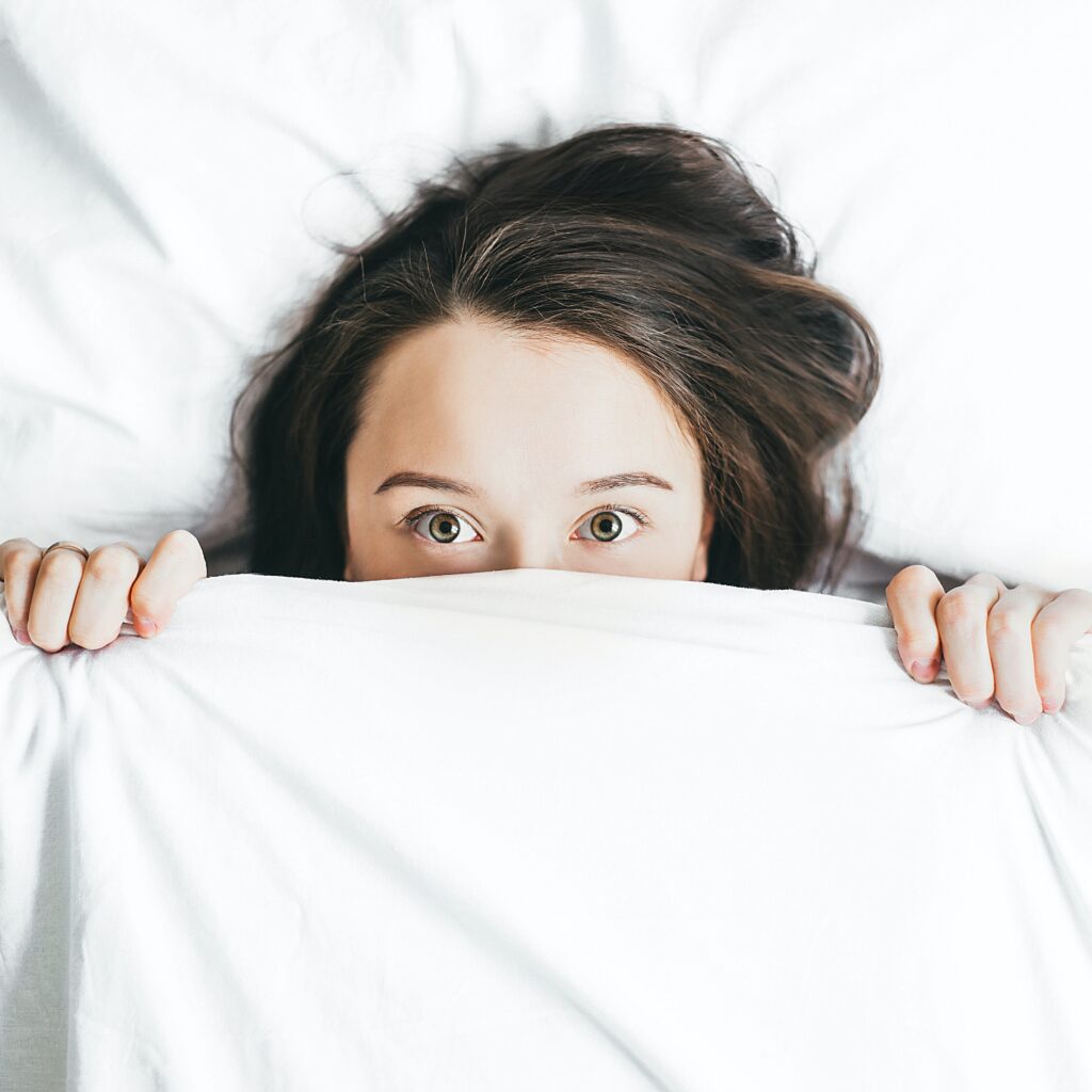 A woman hiding below the blanket in the bed.